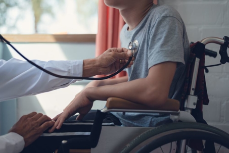 Doctor holding a stethoscope to the chest of a child who has cerebral palsy and is sitting in a wheelchair.